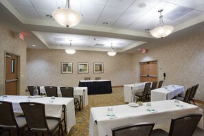 A conference room with tables and chairs, ceiling lights, and framed pictures on the wall.