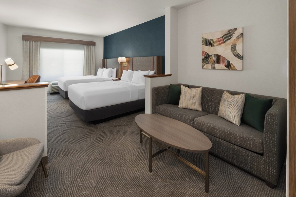 A hotel room with a bed, a sofa, a small table, and a desk with a lamp.