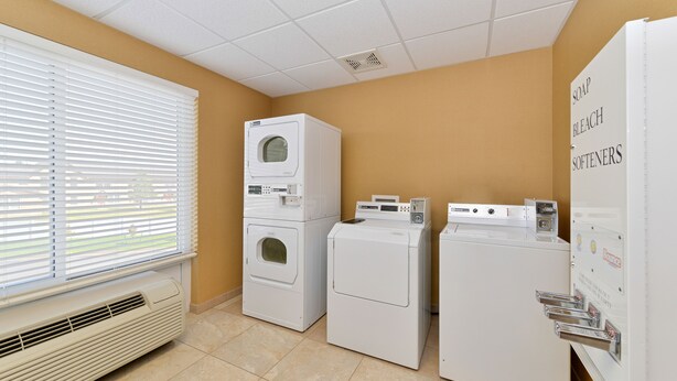 A laundry room with stacked washers and dryers, a vented heater, and a window with blinds. - Holiday Inn Laramie by IHG (Laramie)