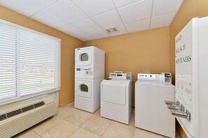 A laundry room with stacked washers and dryers, a vented heater, and a window with blinds.
