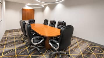 A conference room with a wooden table, black chairs, and a patterned carpet.