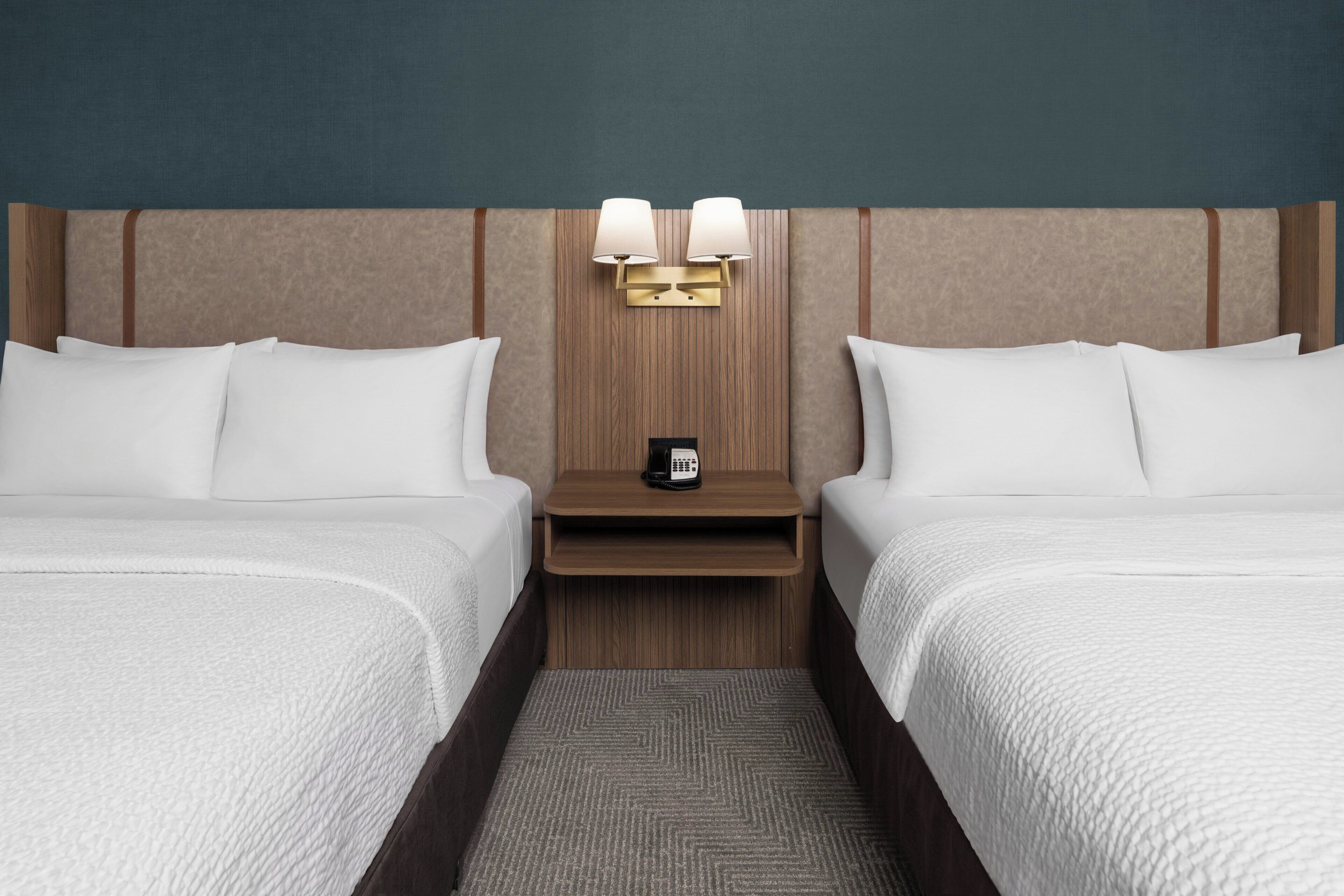Quarto de hotel com duas camas, uma mesa de cabeceira com abajur e um telefone.