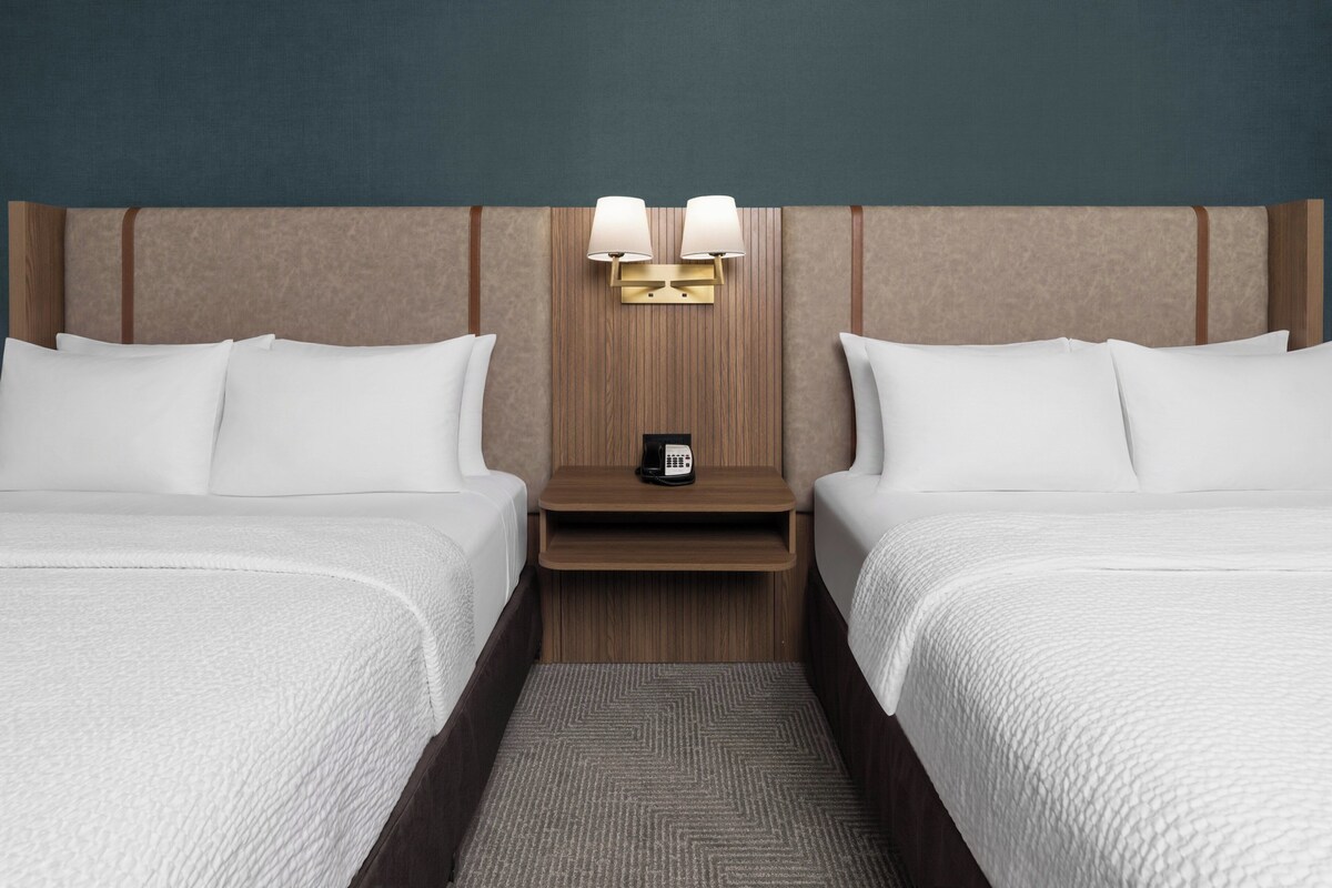 A hotel room with two beds, a nightstand with a lamp, and a telephone.