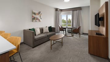 Een hotelkamer met een bank, een eettafel, stoelen, een televisie en een raam met gordijnen.