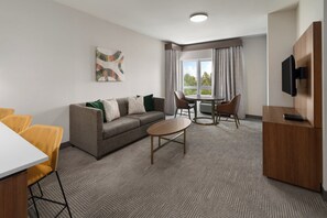 A hotel room with a sofa, a dining table, chairs, a TV, and a window with curtains. - Holiday Inn Laramie by IHG (Laramie)