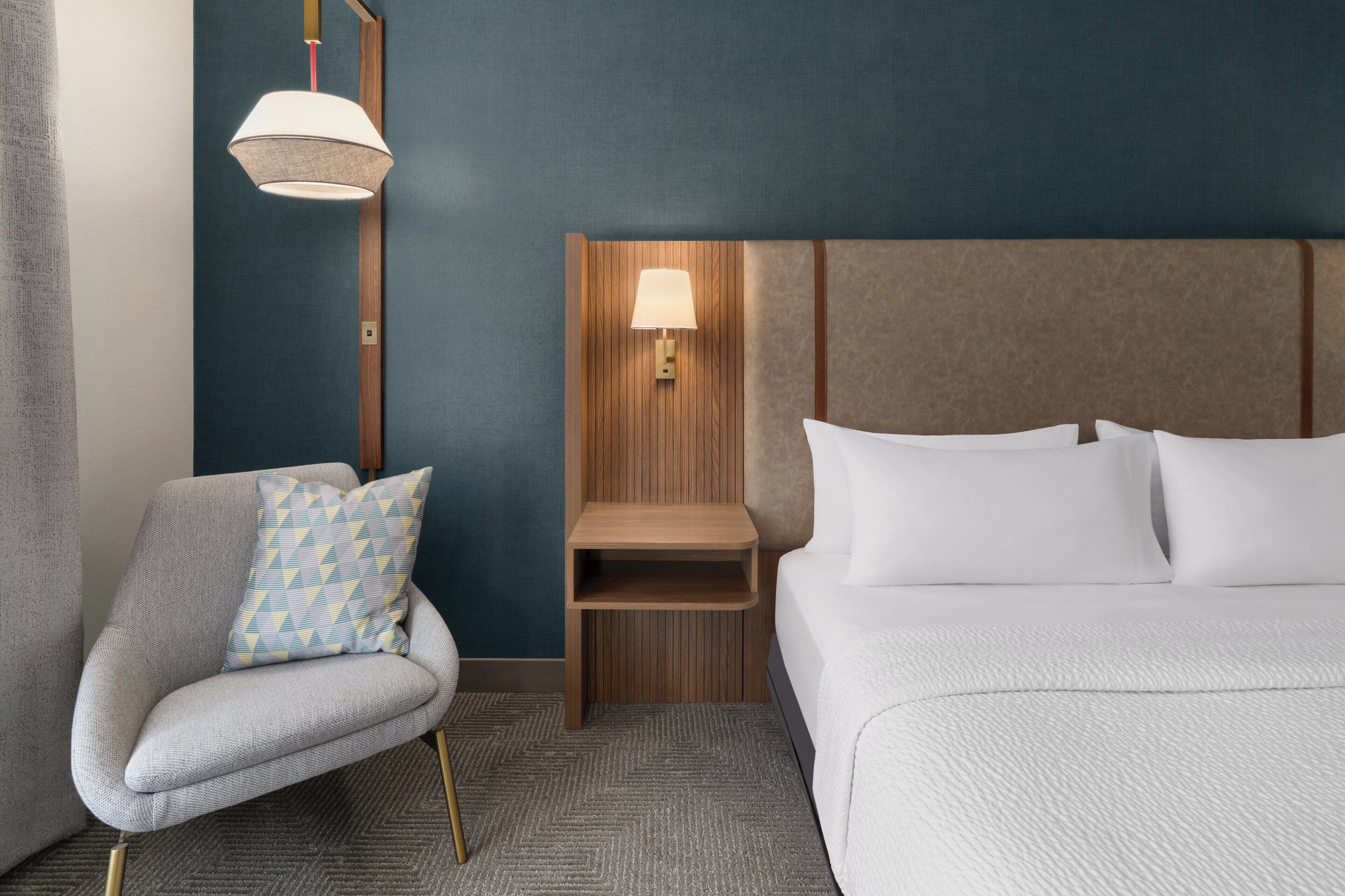 Ein Hotelzimmer mit einem Bett, einem Sessel, einem Nachttisch und einer Wandlampe.