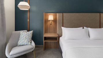 Ein Hotelzimmer mit einem Bett, einem Sessel, einem Nachttisch und einer Wandlampe.