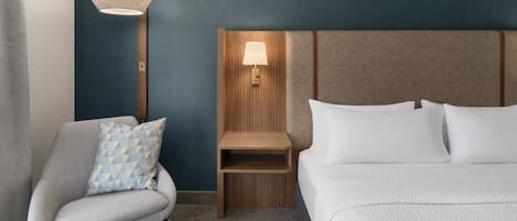 A hotel room with a bed, a chair, a nightstand, and a wall-mounted lamp.