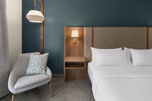 Une chambre d’hôtel avec un lit, une chaise, une table de chevet et une lampe fixée au mur.