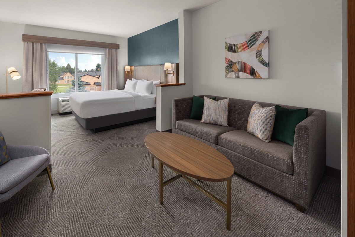 A hotel room with a bed, a sofa, a coffee table, and a painting on the wall.