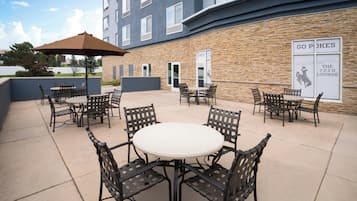 Ein Terrassenbereich im Freien mit runden Tischen und Stühlen, einer Steinmauer und einem Schild für eine Lounge.