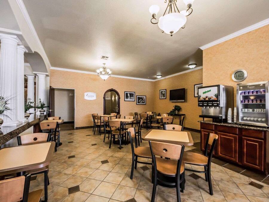 A hotel dining area with multiple tables and chairs, a chandelier, a clock, and a refrigerator with beverages.