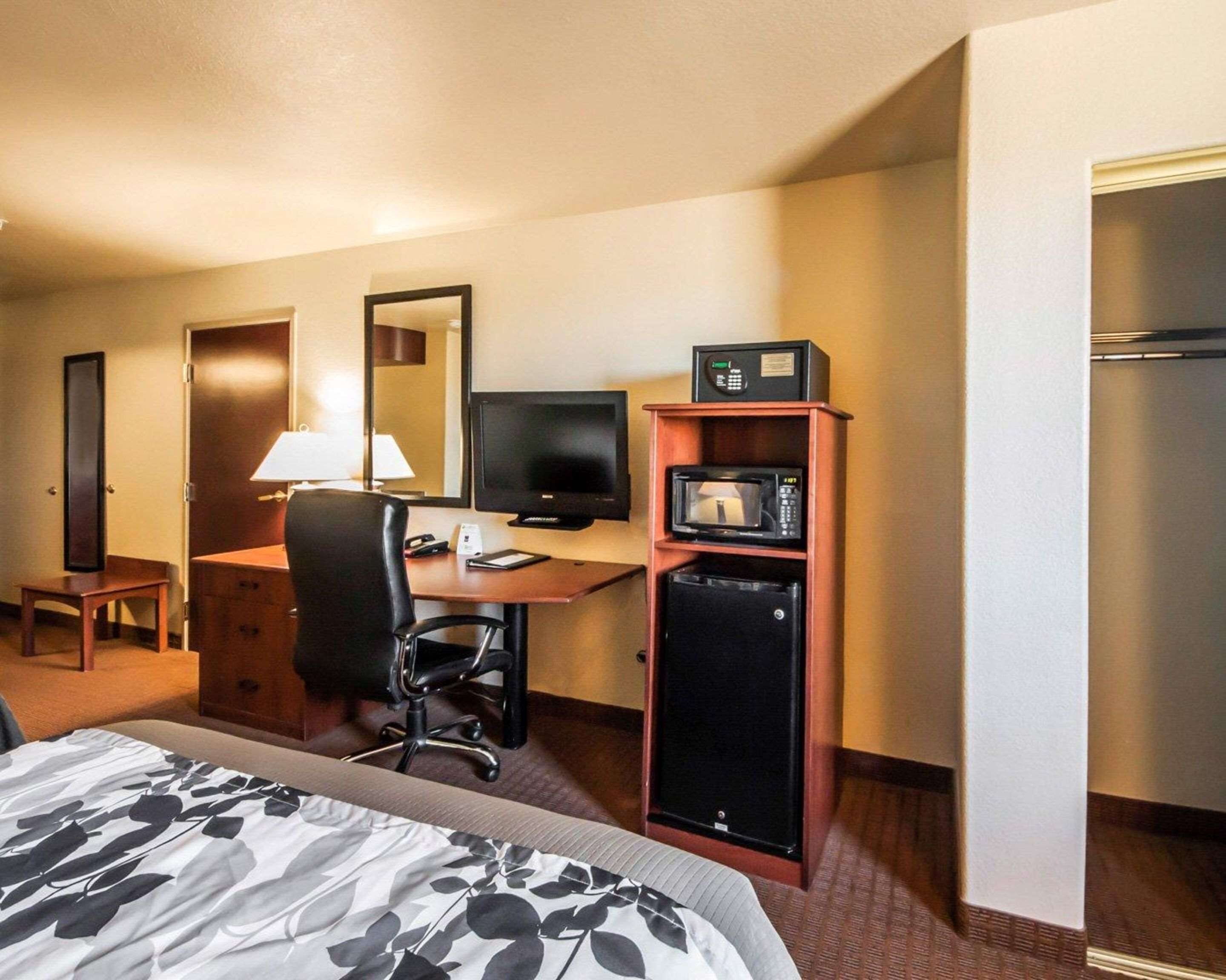 Una habitación de hotel con cama, escritorio, computadora, microondas, refrigerador y espejo.