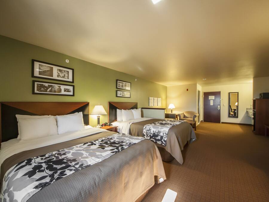 A hotel room with two beds, a desk, a chair, a TV, and framed pictures on the wall.
