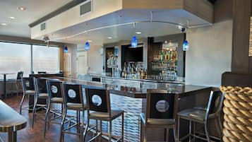 A bar area with multiple bar stools, a bar counter, and a variety of bottles and glasses.