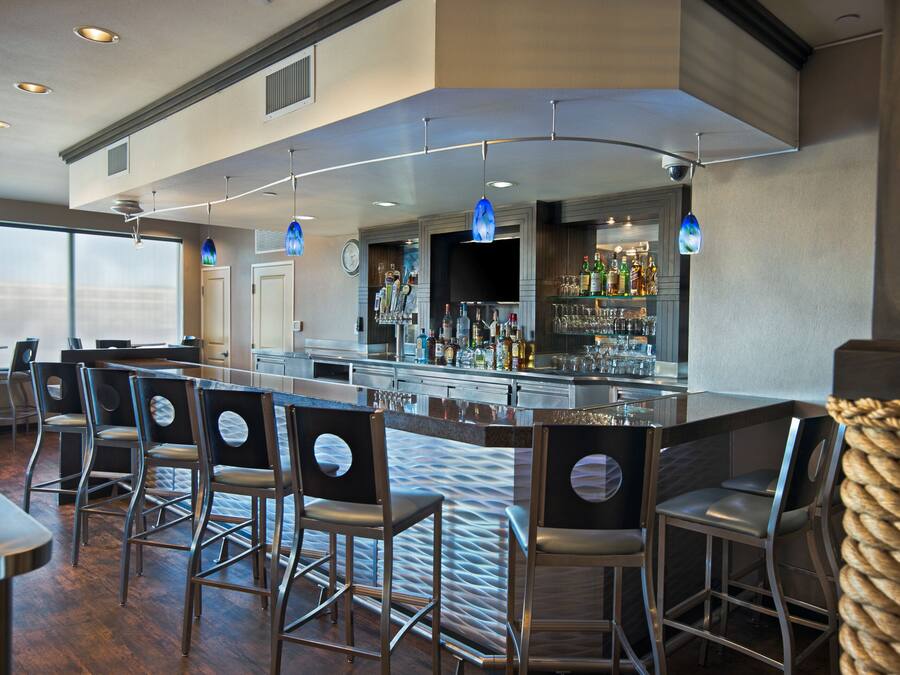 A bar area with multiple bar stools, a bar counter, and a variety of bottles and glasses.