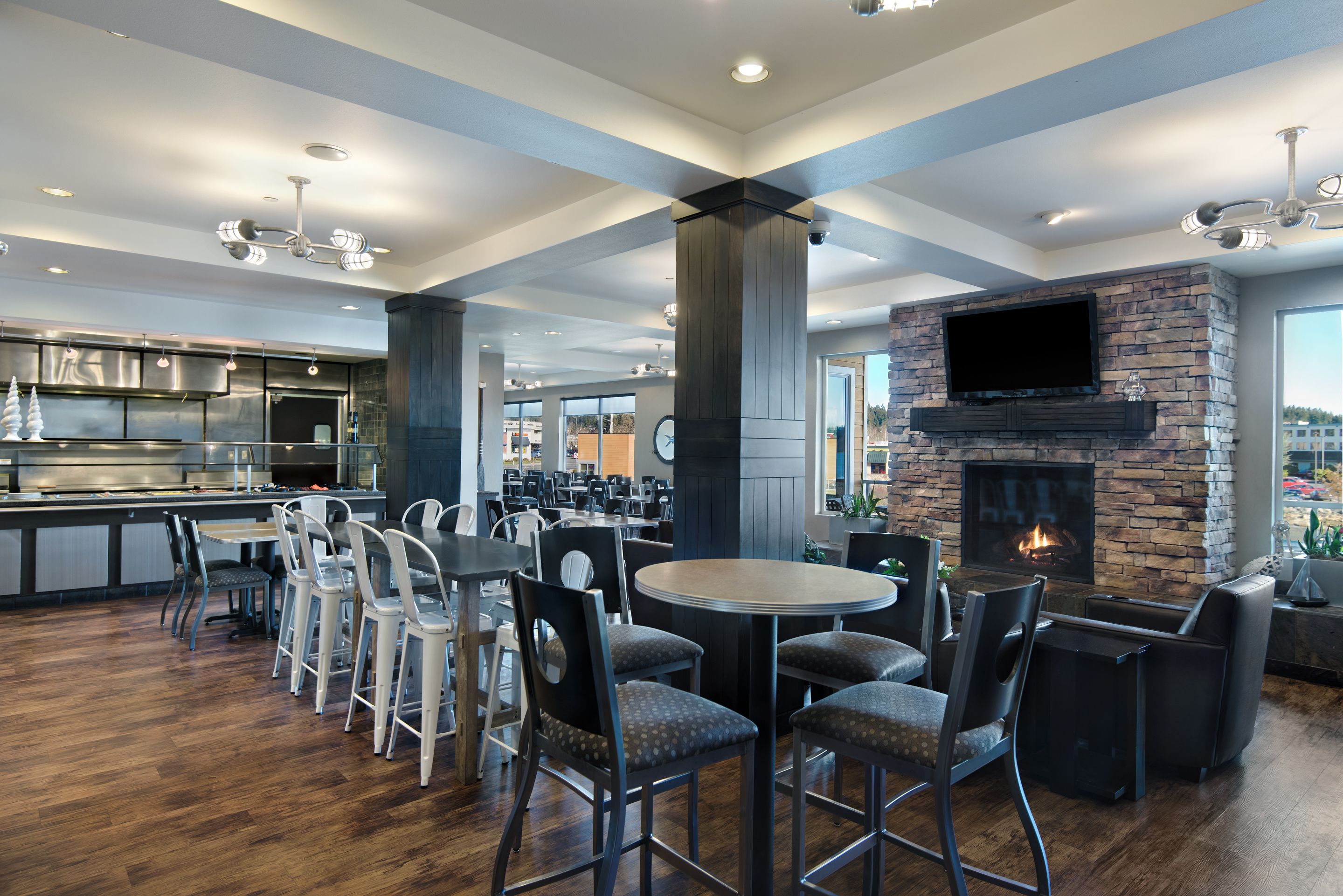 Een modern restaurant met een bar, een open haard en een keuken op de achtergrond.