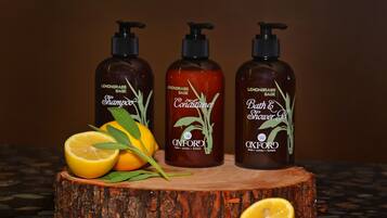 Three bottles of Oxford shampoo, conditioner, and bath & shower gel on a wooden surface with lemons and leaves.