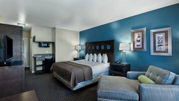A hotel room with a bed, a desk, a TV, a chair, and artwork on the walls.