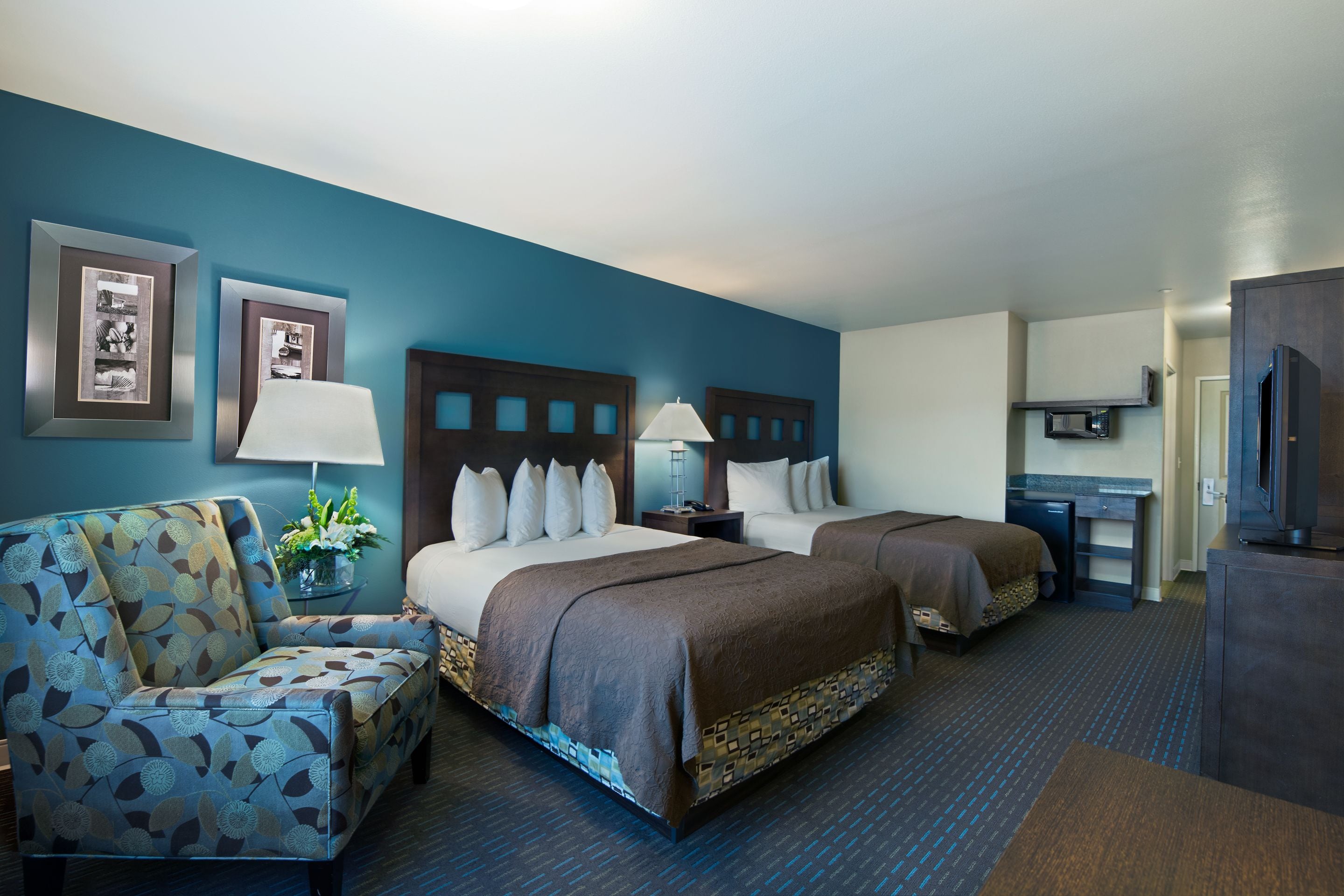 A hotel room with two beds, a sofa, a desk, and a TV.