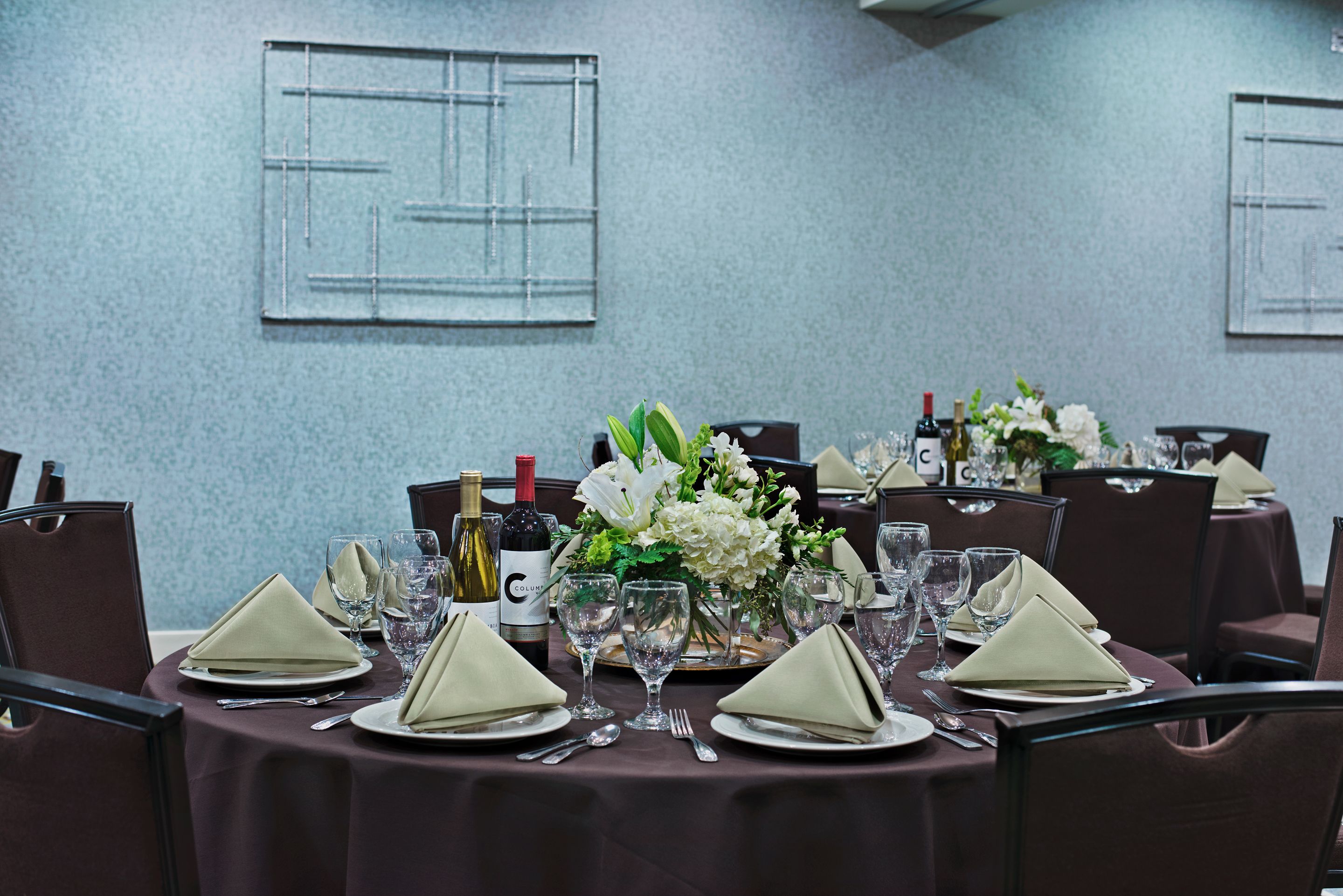 A dining table set with white napkins, wine glasses, and a centerpiece of white flowers.