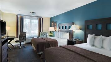 A hotel room with two beds, a desk, a chair, and a TV.