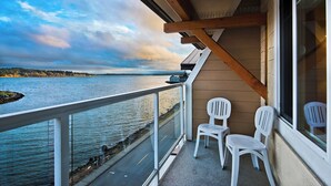 Un balcone con vista su un lago e una costa lontana, con due sedie di plastica bianca e una struttura in travi di legno.
