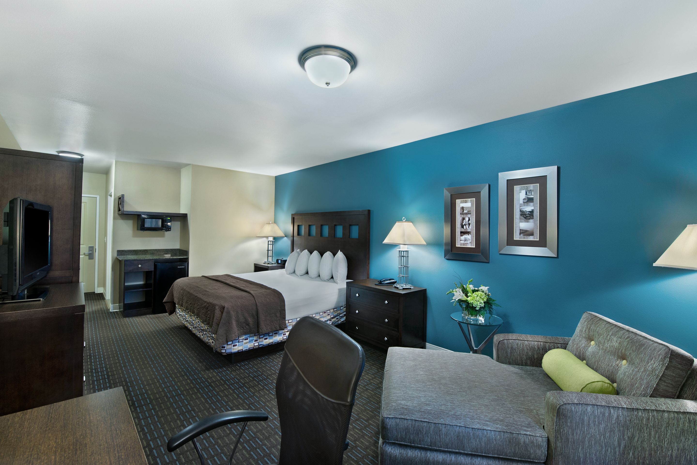 Ein Hotelzimmer mit einem Bett, einem Schreibtisch, einem Sessel, einem Sofa, einem Fernseher und einem kleinen Tisch mit einer Lampe.