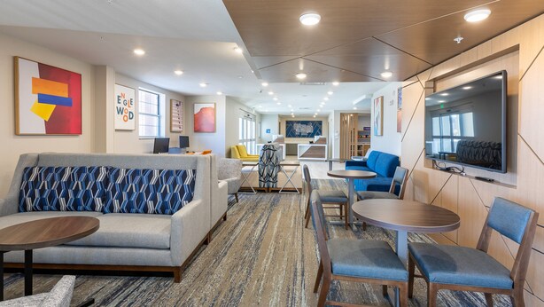 A modern hotel lobby with a sofa, chairs, a coffee table, and a TV screen. - Holiday Inn Express & Suites Englewood Denver South by IHG (Englewood)
