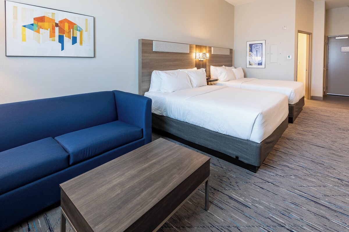 A hotel room with a blue sofa, two beds, a wooden coffee table, and artwork on the walls.