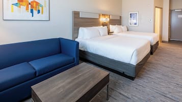 A hotel room with a blue sofa, two beds, a wooden coffee table, and artwork on the walls.