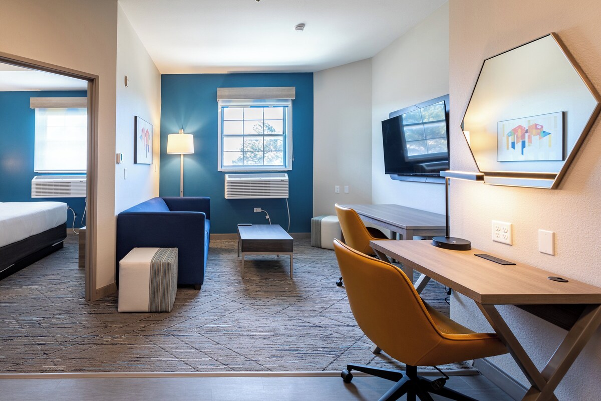 A hotel room with a bed, a desk, a chair, a lamp, and a TV.