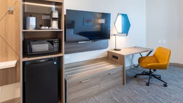 Quarto de hotel compacto com cozinha compacta, televisão de tela plana, escrivaninha e cadeira, e carpete estampado.