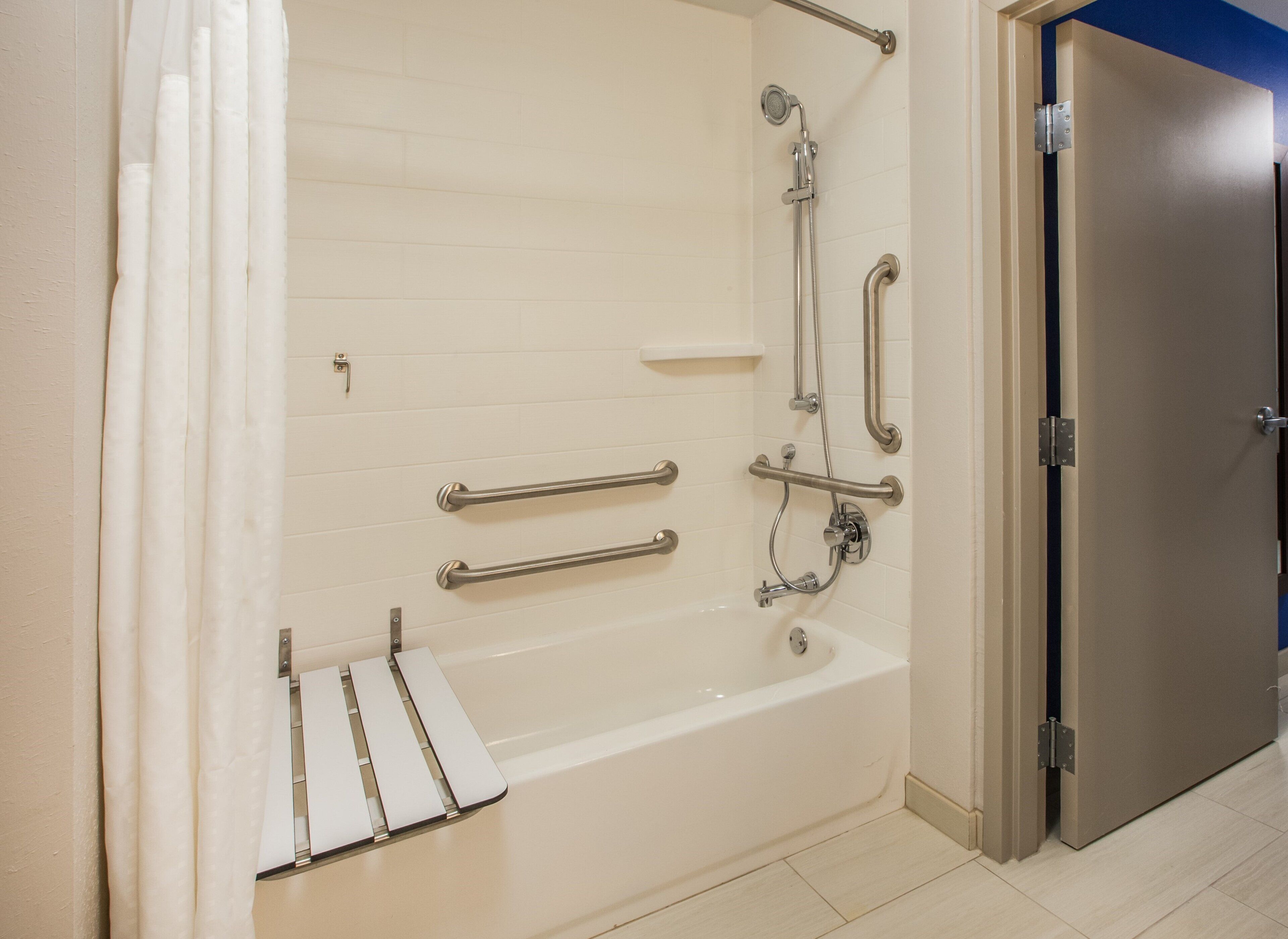 A bathroom with a bathtub, grab bars, a showerhead, and a door.