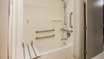 A bathroom with a bathtub, grab bars, a showerhead, and a door.