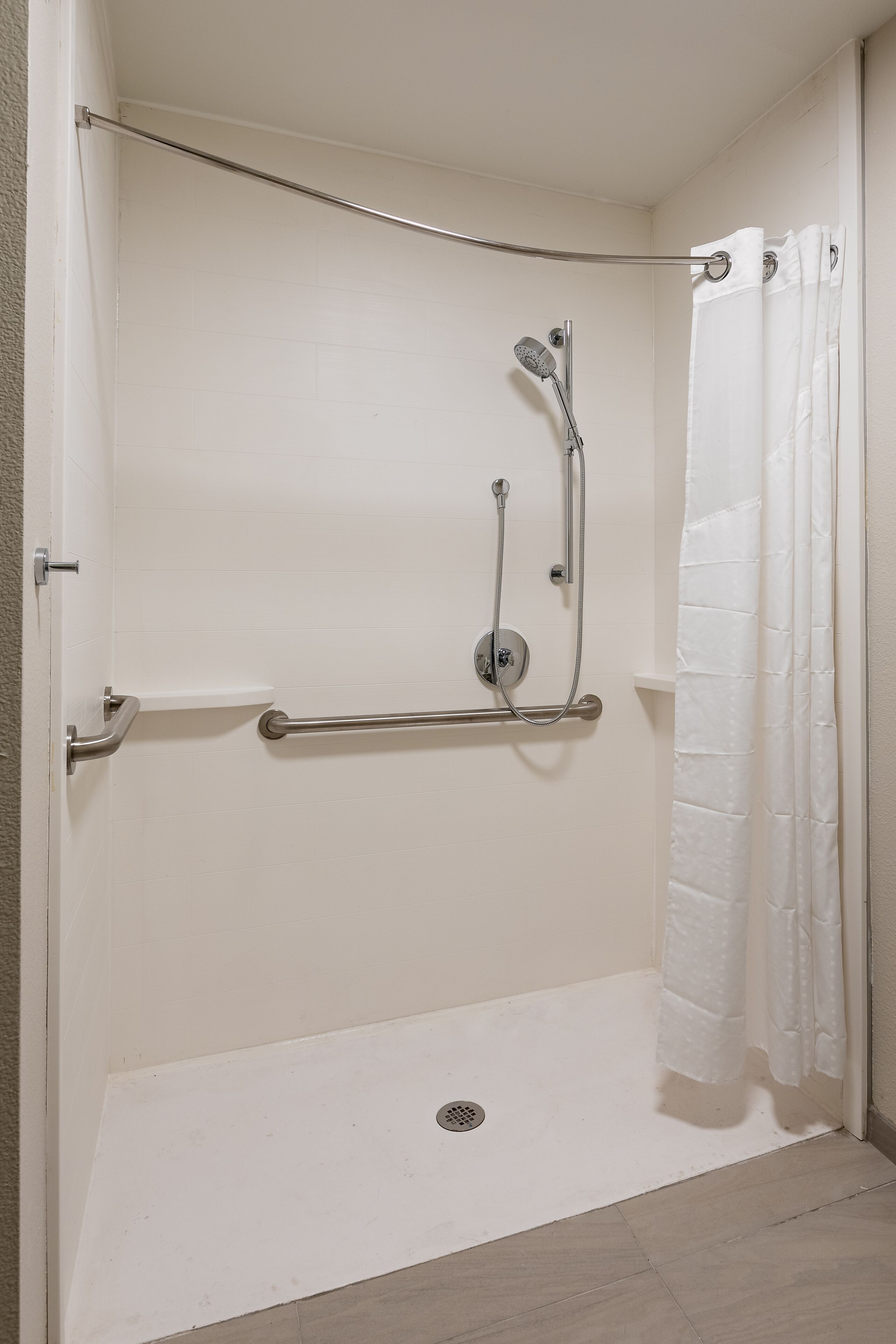 A walk-in shower with a grab bar, a handheld showerhead, and a white shower curtain.