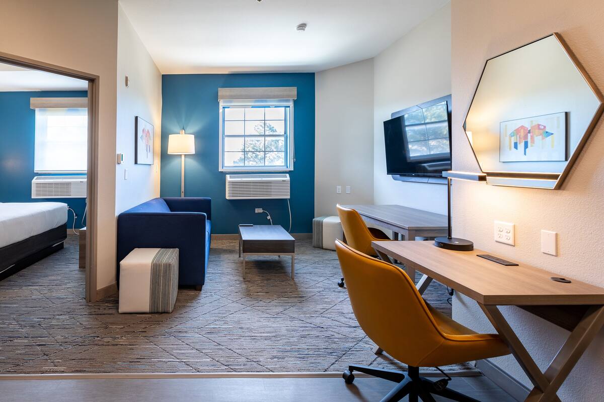 A hotel room with a bed, a desk, a chair, a lamp, and a TV.