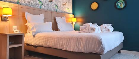 Una cama bien hecha con sábanas y almohadas blancas, una mesita de noche con una lámpara, y una pared con un estampado de pájaros y cuadros enmarcados.