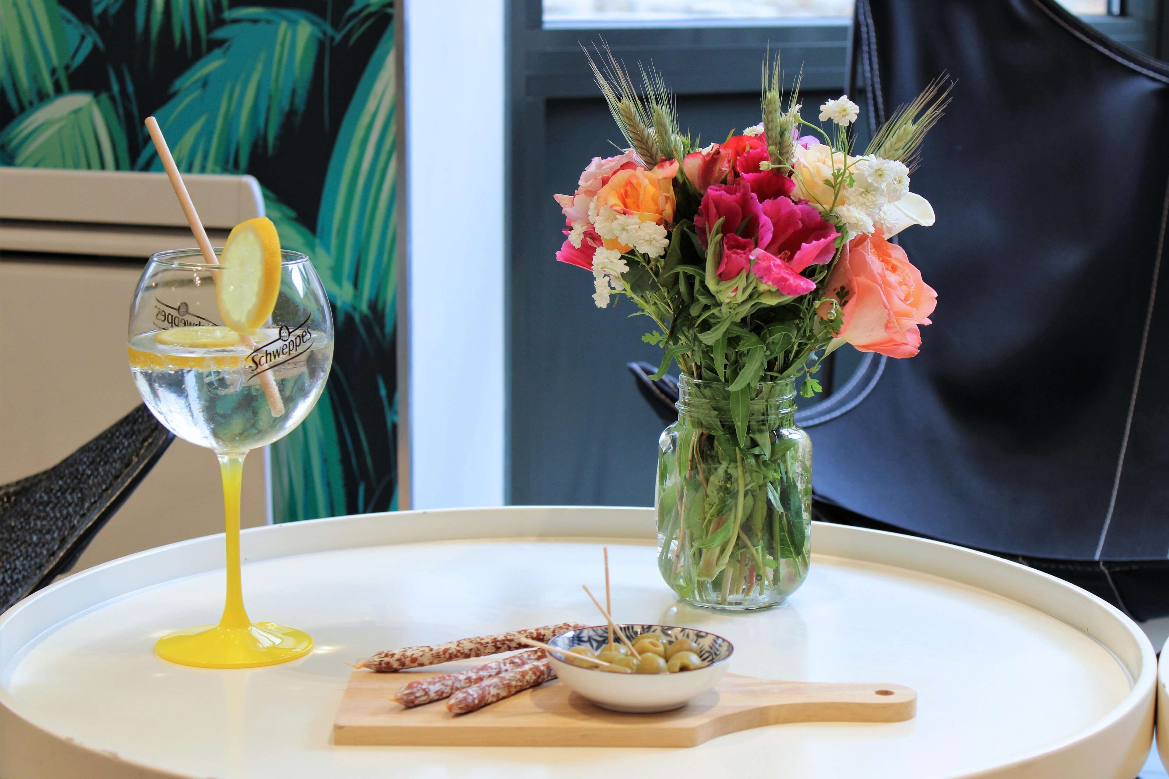 A table with a glass of water, a bowl of olives, and a jar of flowers.