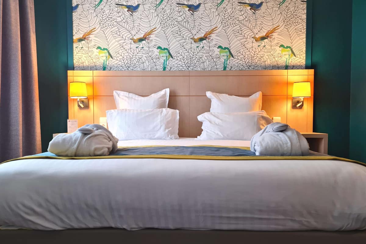 A hotel room with a large bed, two bedside lamps, and a wall with a bird pattern.
