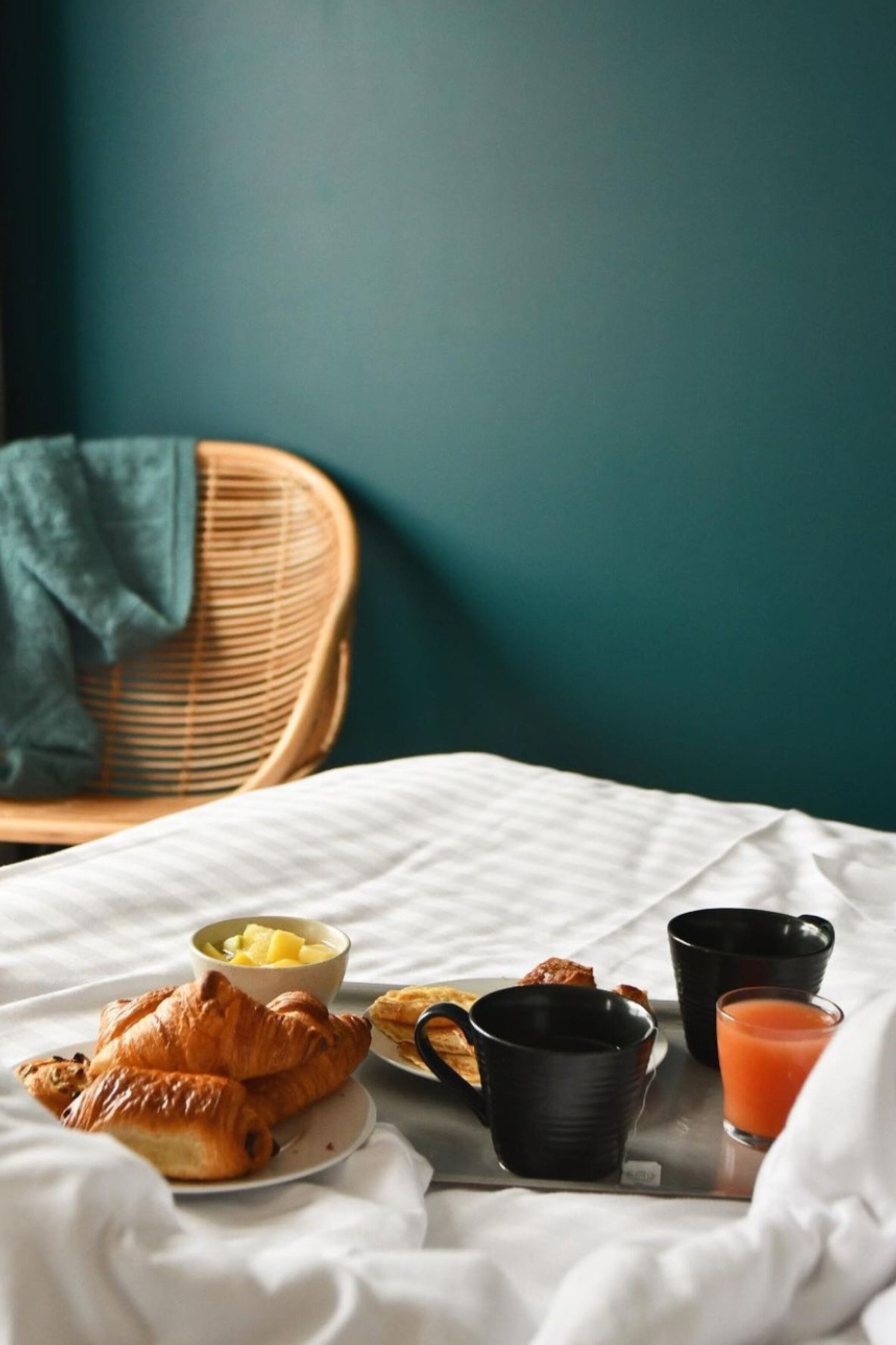 A breakfast setup on a bed with croissants, fruit, and juice.