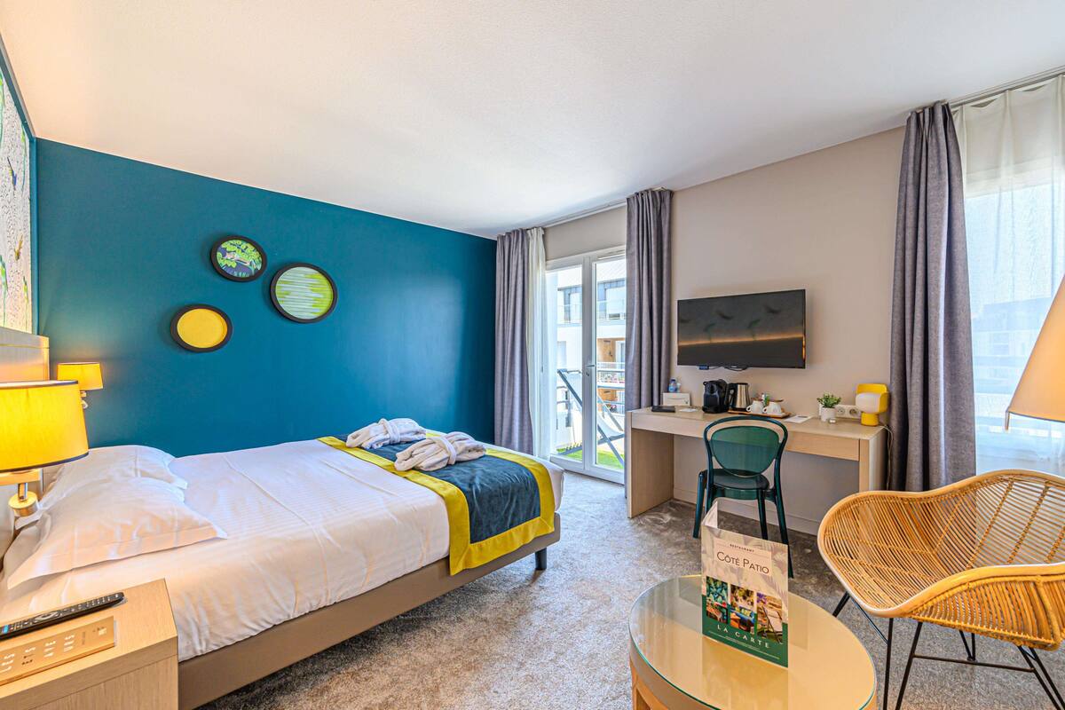 A hotel room with a bed, a desk, a chair, a TV, and a balcony with a view.