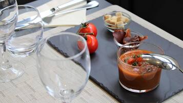 A table with a glass of water, a glass of tomato soup garnished with herbs, a bowl of bread cubes, and a small bowl of bacon.