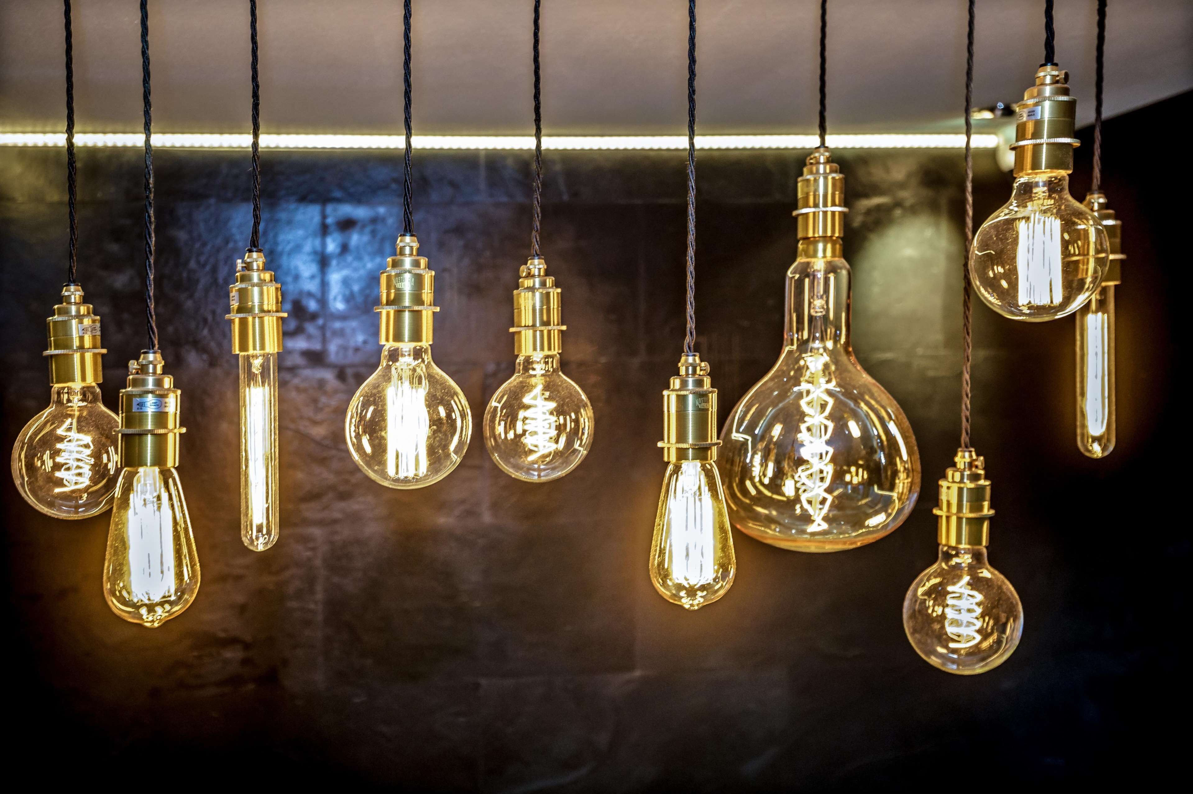 Une série d’ampoules suspendues, dont les filaments sont apparents, maintenues par des cordons noirs sur un fond sombre.