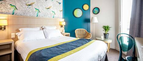 Habitación de hotel con una cama grande, un escritorio, una silla, una pared con un mural de aves y una planta en maceta.