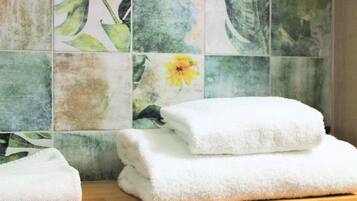 A stack of white towels on a wooden surface against a tiled wall with floral patterns.