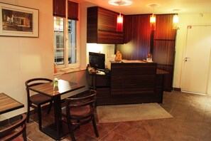 A compact kitchen with dark wood cabinets, a small dining table, and chairs. There is a window with blinds, a refrigerator, and a sink. - Hotel Le Mistral (Cannes)