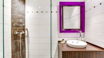 A modern bathroom with a glass shower enclosure, a wooden vanity, and a purple-framed mirror.