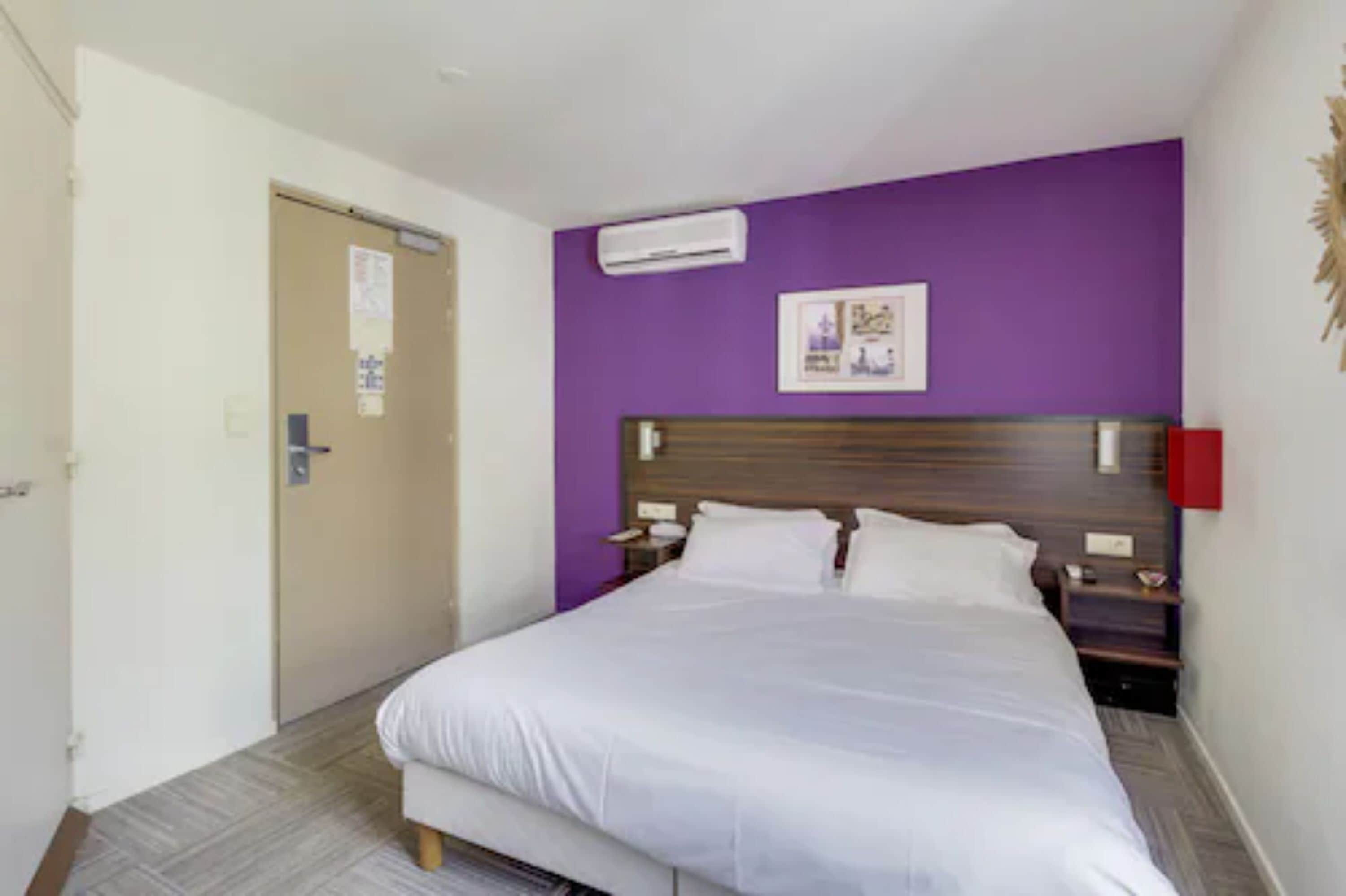 Habitació d'hotel amb llit, una taula de nit, aire condicionat fixat a la paret i una porta amb un senyal.