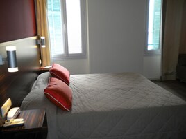Habitación de hotel con cama, mesita de noche con lámpara, teléfono y ventana con cortinas.
